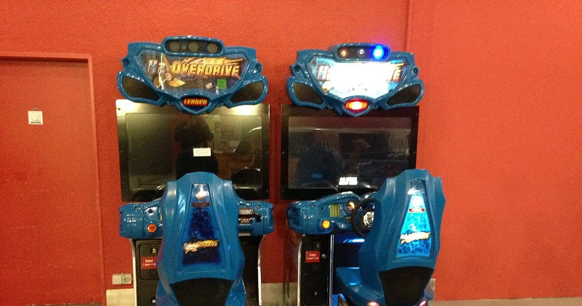 Two arcade racing game cabinets against a red wall
