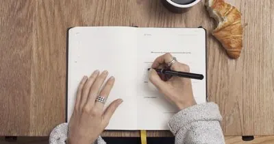 Hands writing in a notebook on a wooden table
