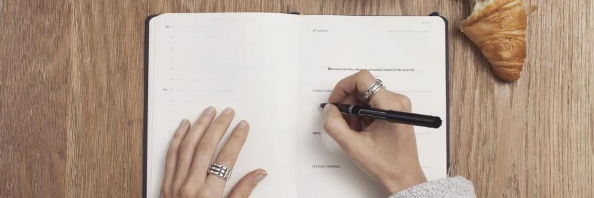Hands writing in a notebook on a wooden table